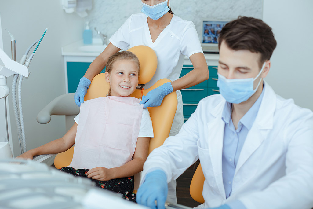 Little girl in dental chair with dentists wearing face masks